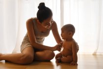 Beautiful happy young mothe with adorable infant child in diaper sitting together on floor and playing at home — Stock Photo