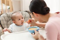 Jovem asiático mulher alimentação bonito bebê em casa — Fotografia de Stock