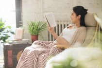 Side view of smiling young pregnant woman sitting in chair and reading book, selective focus — Stock Photo