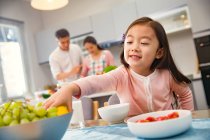 Adorabile bambino mangiare frutta mentre i genitori cucinano dietro in cucina — Foto stock