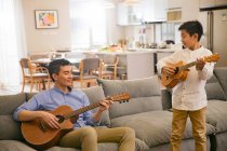 Feliz asiático pai e filho tocando guitarras juntos em casa — Fotografia de Stock