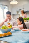 Pai feliz e filha tomando café da manhã juntos, sorrindo mãe de pé atrás na cozinha — Fotografia de Stock