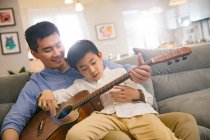Счастливый азиатский отец и сын вместе играют на акустической гитаре дома — стоковое фото
