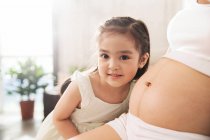 Adorable happy little girl listening to belly of pregnant mother, cropped shot — Stock Photo