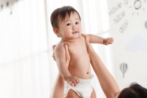 Cortado tiro de jovem mãe carregando adorável asiático bebê em fralda em casa — Fotografia de Stock