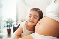 Adorable happy little girl hugging and listening to belly of pregnant mother at home, cropped shot — Stock Photo