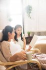 Happy pregnant mother and little daughter reading book together at home — Stock Photo