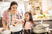 Schöne glückliche junge Mutter mit entzückender kleiner Tochter, die gemeinsam in der Küche kocht — Stockfoto