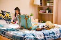 Carino poco asiatico ragazza imballaggio valigia su letto — Foto stock