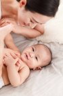 Высокий угол зрения счастливой молодой азиатской матери и очаровательный младенец, лежащих вместе на кровати — стоковое фото