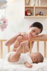 Happy young mother playing with adorable infant baby lying in crib — Stock Photo