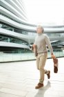 Piena lunghezza vista di maturo asiatico businessman holding valigetta e walking fuori ufficio edificio — Foto stock