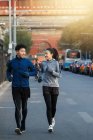 Young asian athletes in sportswear smiling each other and jogging together on street — Stock Photo