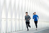 Усміхнені молоді чоловіки і жінки спортсмени бігають разом на сучасному мосту — стокове фото