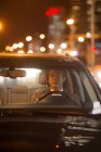 View through windshield of serious mature asian man driving car at night — Stock Photo