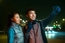Glückliche sportliche junge asiatische Paar macht Selfie mit Smartphone während des Trainings in der Nacht — Stockfoto