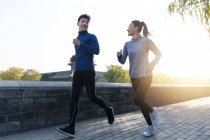 Bajo ángulo vista de joven asiático pareja en sportswear sonriendo uno al otro y corriendo juntos en la mañana - foto de stock