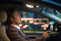 Vista lateral de sério maduro asiático empresário condução carro à noite — Fotografia de Stock