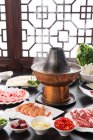 Copper hot pot and plates with meat, shrimp and vegetables on table, chafing dish concept — Stock Photo