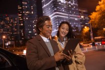Щаслива азіатська пара дивиться на планшет біля машини ввечері — стокове фото