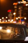 Vista a través del parabrisas de hombre asiático maduro conduciendo coche por la noche - foto de stock