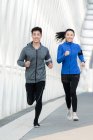 Glückliche junge asiatische Jogger lächeln in die Kamera und laufen zusammen auf einer Brücke — Stockfoto