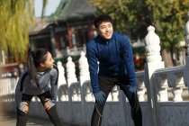 Sorrindo jovem asiático corredores alongamento e descansando durante o treino ao ar livre — Fotografia de Stock