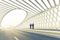 Полный вид молодого спортсмена и спортсменки, бегущих вместе по современному мосту — стоковое фото