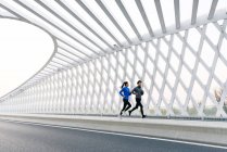 Side view of young asian male and female athletes running together on bridge — Stock Photo
