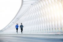 Full length view of young asian male and female athletes running together on bridge — Stock Photo