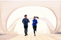Ganzkörperansicht eines jungen asiatischen Paares in Sportbekleidung, das sich gegenseitig anlächelt und gemeinsam auf einer Brücke läuft — Stockfoto