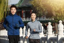 Feliz jovem asiático casal sorrindo para câmera e correndo juntos na rua — Fotografia de Stock