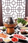 Cropped shot of person with chopsticks holding meat above copper hot pot, chafing dish concept — Stock Photo