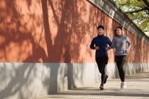 Full length view of smiling young asian sportsman and sportswoman running together on street — Stock Photo