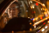 Sérieux mature asiatique l'homme assis dans voiture la nuit, sélectif focus — Photo de stock