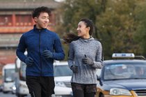 Happy sporty young asian couple smiling each other and running together on street — Stock Photo