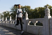 Vista completa de hermosa joven asiática mujer en ropa deportiva corriendo en la calle - foto de stock
