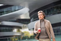 Ältere asiatische Geschäftsmann halten Kaffee zu gehen und zu Fuß auf der Straße — Stockfoto