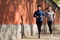 Улыбающиеся молодые азиатские спортсмены, бегущие вместе по улицам — стоковое фото