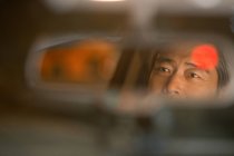 Отражение в зеркале зрелого азиатского мужчины за рулем автомобиля, крупным планом, избирательным фокусом — стоковое фото