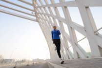Baixo ângulo vista de sorrir jovem asiático mulher no sportswear correndo na ponte — Fotografia de Stock