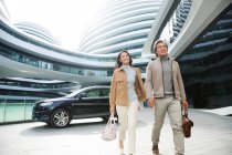Веселые азиатские бизнесмены, идущие рядом с парковкой в современном бизнес-центре — стоковое фото