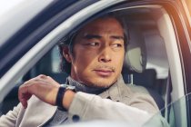 Primer plano vista de maduro asiático hombre sentado en coche y mirando lejos - foto de stock