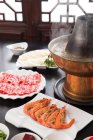 Vista de cerca de camarones y carne en platos y olla caliente de cobre, concepto de plato de roce - foto de stock