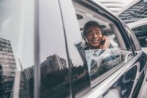 Smiling mature asian businessman sitting in car and talking by smartphone — Stock Photo