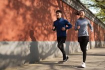 Вид в полный рост спортивной молодой пары, бегущей вместе по улице — стоковое фото