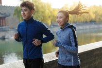 Sonriente joven asiático macho y hembra corredores entrenamiento juntos al aire libre - foto de stock