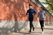 Visão comprimento total do jovem casal desportivo correndo juntos na rua — Fotografia de Stock