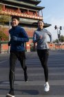 Sonriendo joven asiático hombre y mujer corriendo juntos en la calle - foto de stock