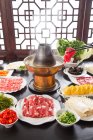 Chopsticks with meat above copper hot pot and plates with various ingredients on table, chafing dish concept — Stock Photo